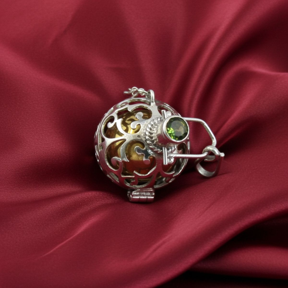 Silver filigree pendant with a green gemstone on a red satin background