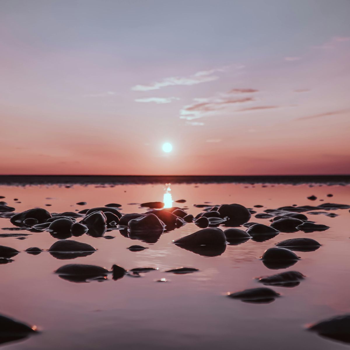 Sunset over a body of water with rocks in the foreground
