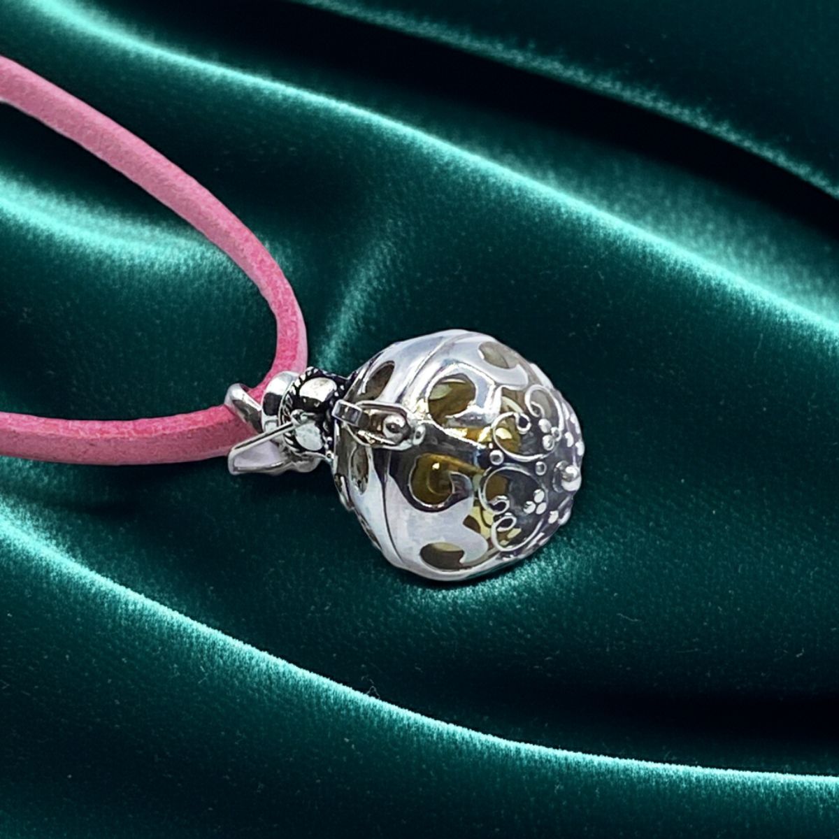 Silver pendant on a pink cord against a green satin background