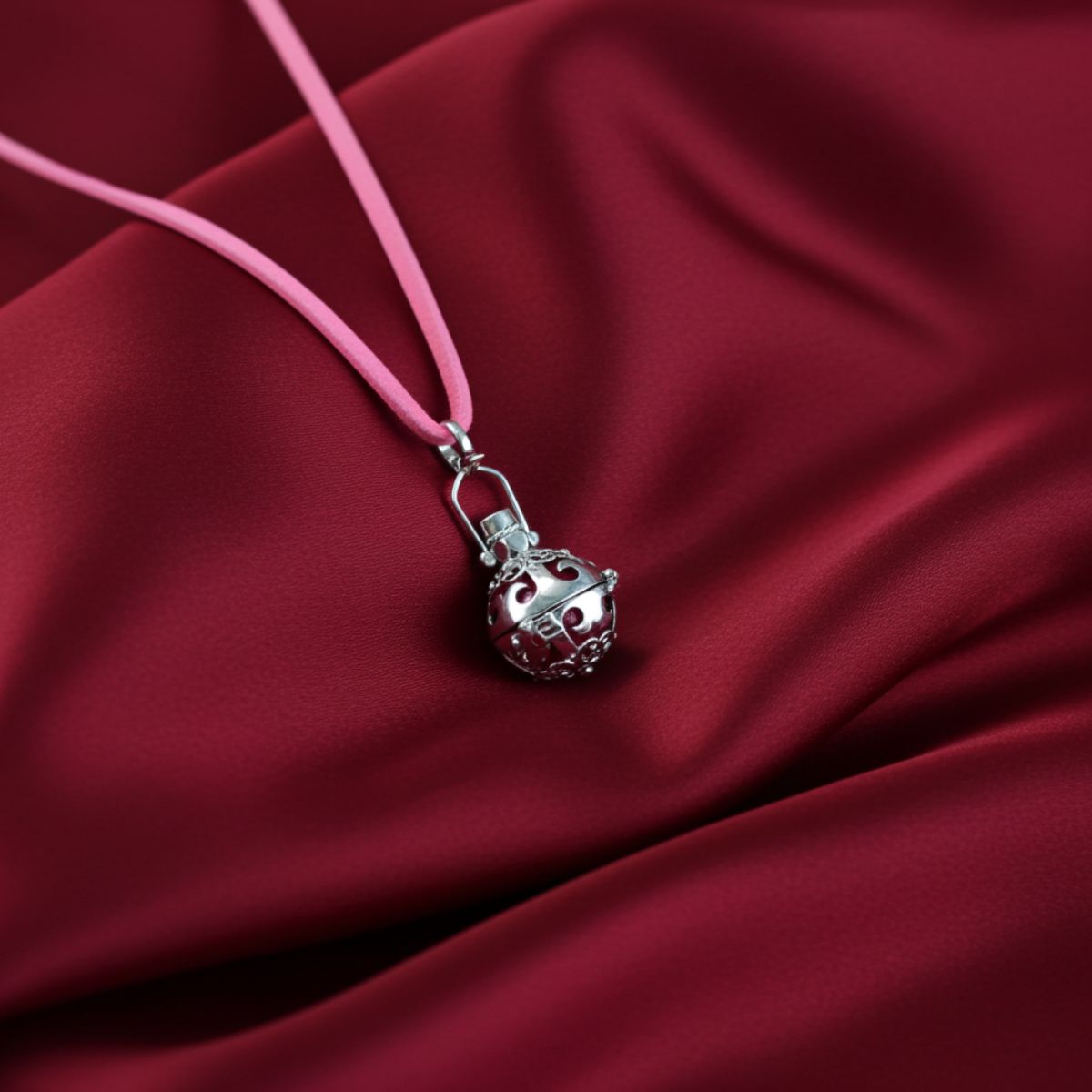 Pink necklace with a silver pendant on a red fabric background