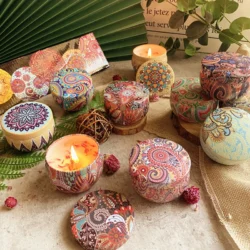 Vintage Flower Candle Jars Soy Wax Fragrance Candles, featuring colorful paisley and mandala designs, are displayed on a rustic surface with some lit among dried flowers and textured fabric, creating a cozy setting.