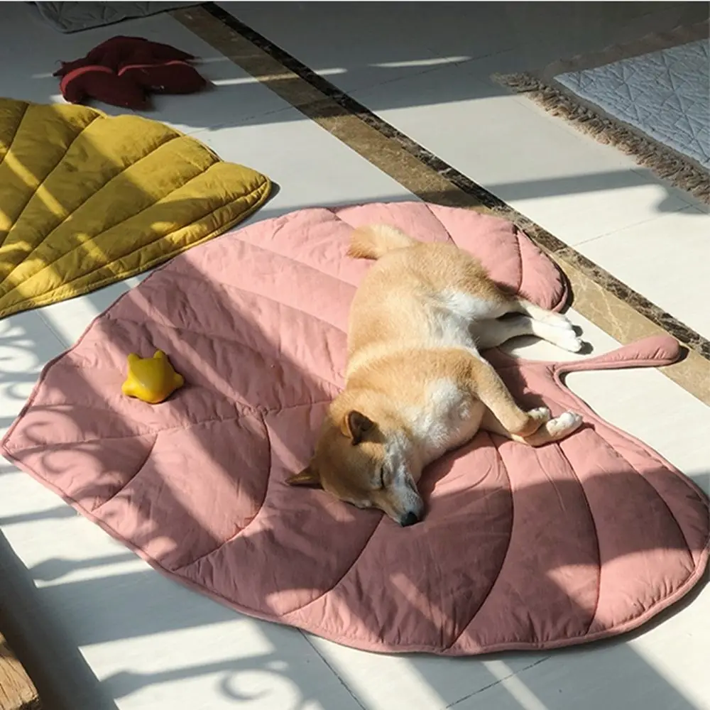 A light brown and white dog sleeps on a pink Dog Cooling Leaf Mat, perfect for summer, on a sunlit tile floor. A small yellow rubber duck toy is beside the dog. Nearby are a yellow Dog Cooling Leaf Mat and a beige textured rug.