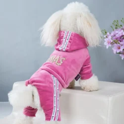 A fluffy white dog sits on a light-colored ottoman, wearing the Puppy Girl Hoodies Jumpsuit with white stripes and glittery gold letters on the hood. A touch of purple flowers in the background adds charm to this stylish look.