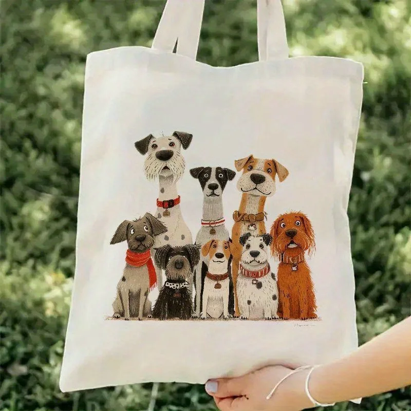 A hand holds the Cute Dogs Print Tote Bag, showcasing eight adorable, varied pups in two rows. The white tote features dogs of different sizes, colors, and collars against a blurred grassy background.