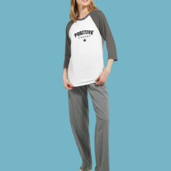 Woman wearing a white and grey raglan T-shirt with black text reading ‘Positive Energy’ and a star design, standing against a blue background.