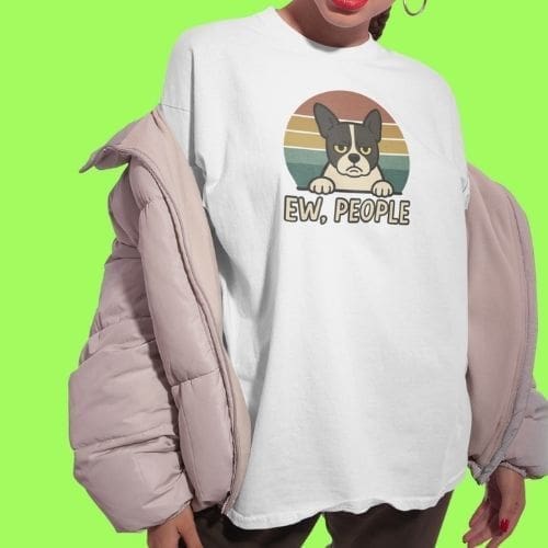 Wearing the Ew, People T-shirt, a person stands with a light pink puffer jacket draped over their shoulders in front of a vibrant green backdrop.