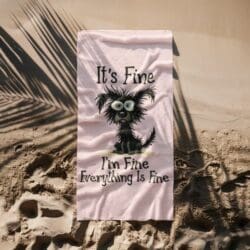 A pale pink beach towel on sand with palm shadows, featuring a cartoon black dog with wild fur and wide eyes. Above and below the dog, text reads: Its Fine. Im Fine. Everything Is Fine.