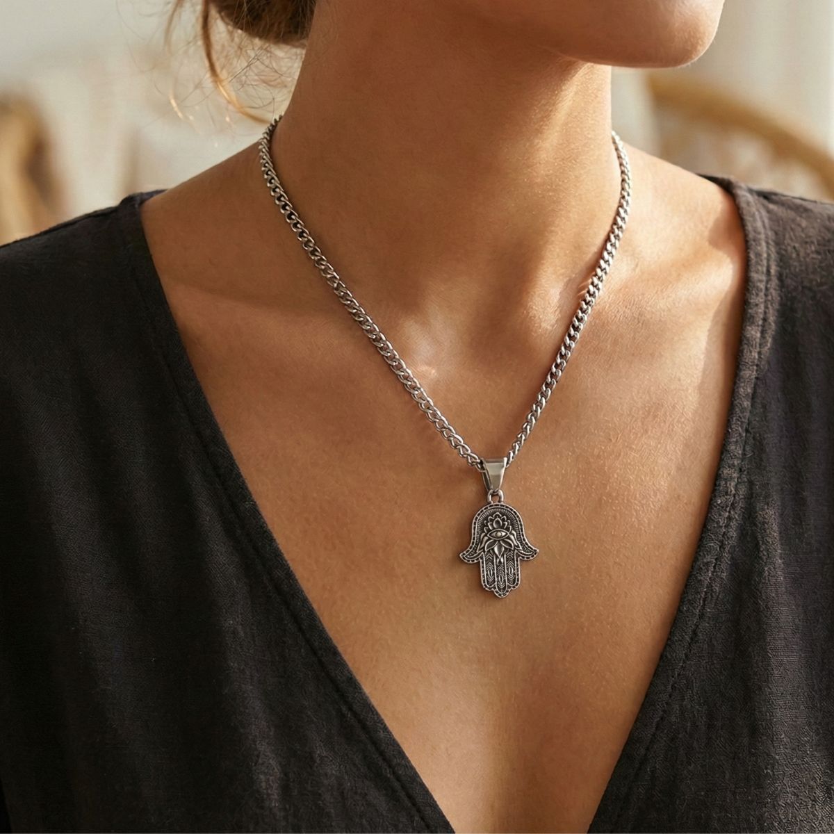 A person wears the Hamsa Hand of Fatima Pendant on a silver chain, with their light skin and black V-neck top highlighting the striking jewelry against a softly blurred background.