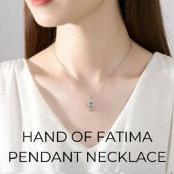 A woman with straight brown hair wears the Turkish Crystal Hand Pendant Necklace featuring a small Hand of Fatima. She is in a white top, drawing attention to her neckline and jewelry. Text: “HAND OF FATIMA PENDANT NECKLACE.”.