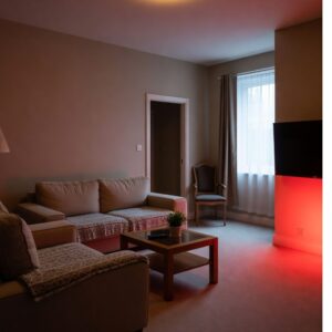 A cozy living room with beige walls, two tan sofas with patterned throws, a wooden coffee table with a plant, and a wall-mounted TV glowing with red light, perfect for an evening routine in a warm atmosphere.