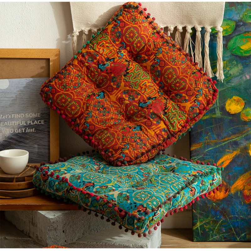 Square orange and turquois bohemian-style cushion with colourful patterned fabric and pom-pom trim around the edges.