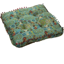 Square turquoise bohemian-style cushion with intricate multicoloured patterns and small pom-pom trim around the edges.