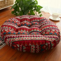 Round red bohemian meditation cushion with geometric patterns placed on a wooden floor near a plant and cup of tea.