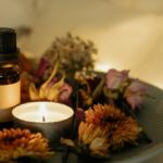 A small brown glass bottle with a black cap and blank label sits on a plate surrounded by dried flowers. A lit tealight candle glows beside it, creating a cosy ambience—perfect as one of your mindfulness gifts for mindful living.