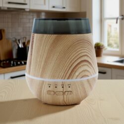 A Wood-Effect Aroma Diffuser – Natural Oak Finish (USB) with a dark translucent top and ON, 1H, 3H, 6H buttons sits on a matching kitchen worktop, framed by cupboards and a window in the background.