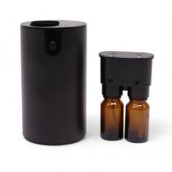 A black, cylindrical waterless essential oil nebuliser sits next to a dual-bottle attachment holding two brown glass bottles with black tops. The diffuser features a small circular button, while the bottles are designed to fit into the nebuliser.
