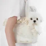 A small white dog looks out from a Cute Lace Carrier Bag for Dogs with ruffled trim, carried over the shoulder by someone in a white short-sleeve shirt against a bright, plain background.