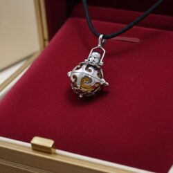 The Silver Angel Bell Necklace – Dreams features an 18mm artisan sterling silver bell with gold filigree, suspended from a black cord and nestled in a red velvet jewelry box. The spherical pendant showcases intricate metalwork and a clasped top.