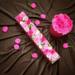 The Luxury Flower Gift Box (Everlasting Roses) – Pink Blessings features pink and white roses and carnations in elegant pink boxes, artfully arranged on brown satin with scattered flower heads for a romantic touch.