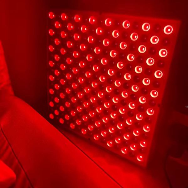 Close-up of the Radiance Panel red light therapy device glowing softly in a warm red hue beside a sofa, creating a calm home ambience.